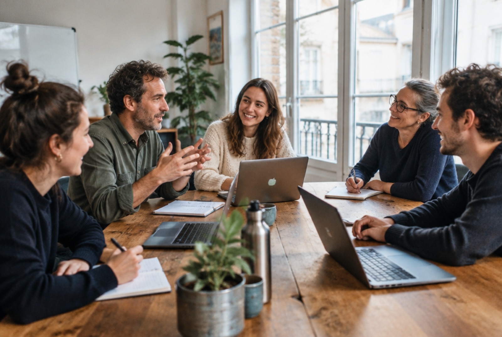 Une petite équipe suit une formation autour d'une grande table, ordinateurs ouverts