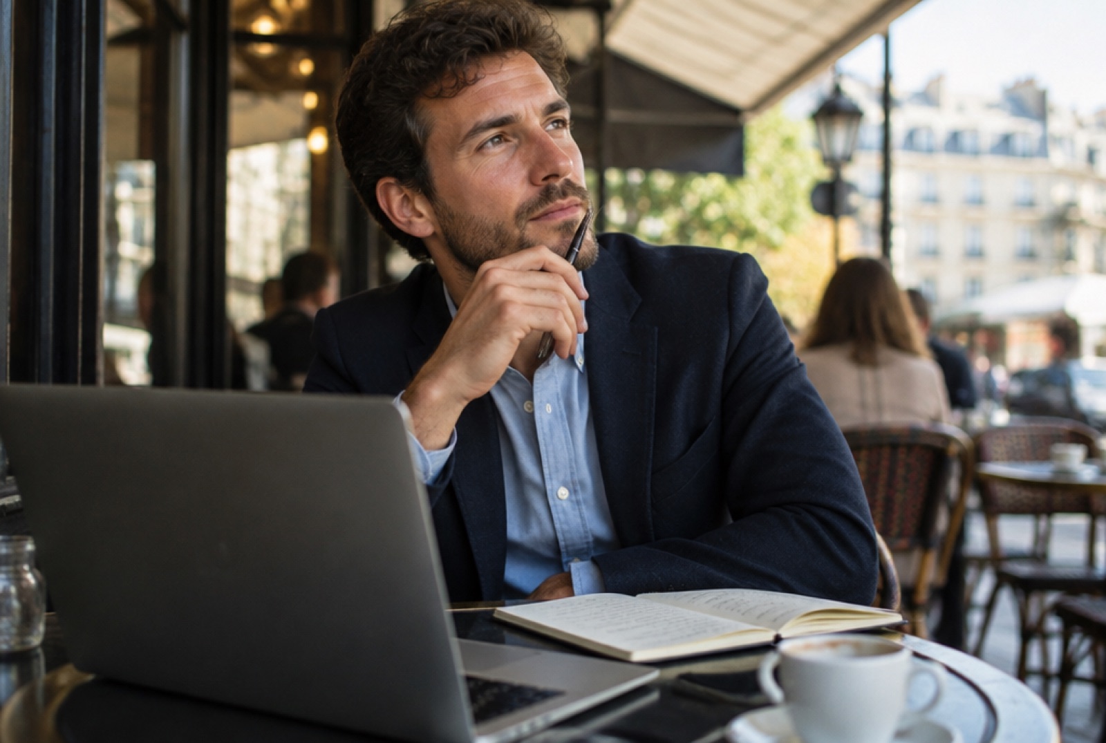 Un agent immobilier réfléchit à la terrasse d'un café, son ordinateur et un carnet devant lui